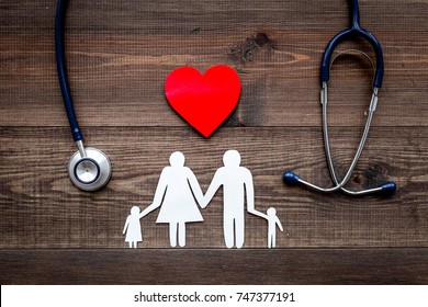 Take out health insurance for family. Stethoscope, paper heart and silhouette of family on wooden background top view