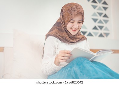 Take a peek at a beautiful hijab girl relaxing while reading a book in the bedroom