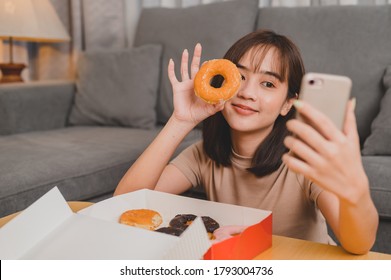 Take Photo Of Donut For Social Online Site. Fast Food Delivery And Takeaway Back Home. Eating Donut When Takeout And Delivery. Asian Woman Lifestyle In Living Room.