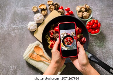 Take a photo of spaghetti with a mobile phone,Top view of woman taking photo on dishes - Powered by Shutterstock