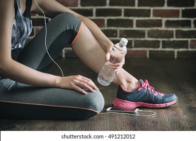 take rest listening to music drinking water after fitness exercise, sitting on wooden floor