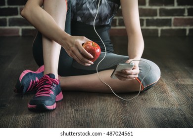 take rest listening to music eating apple after fitness exercise, sitting on wooden floor, healthy lifestyle - Powered by Shutterstock