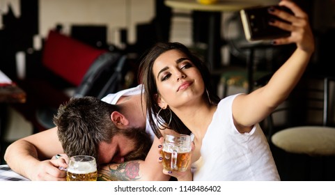 Take selfie to remember great event. Woman making fun of drunk friend. Man drunk fall asleep table and girl with full beer glass. Girl taking selfie photo drunk boyfriend. He appears too weak for her. - Shutterstock ID 1148486402