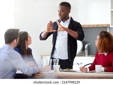 Take A Step Back.... Cropped Shot Of A Young Businessman Addressing His Colleagues During A Business Meeting.