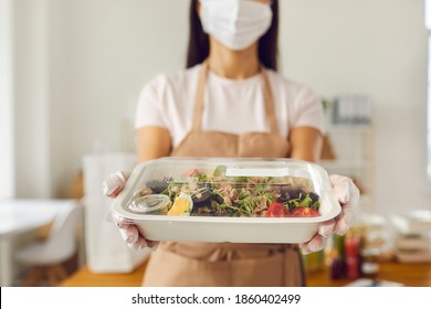 Takeaway Cafe Worker Wearing Medical Face Covering Mask Holding Fresh Healthy Lunch In Plastic Food Container Ready For Safe Delivery. Concept Of Ordering Meal, Good Service And Taking Care Of Clients