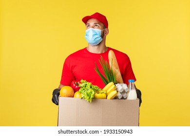 Takeaway Delivery, Food And Drinks, Covid-19 Quarantine And Groceries Concept. Courier Looking Up At Building, Bring Order Grocery Box To Home Or Office, Wearing Protective Medical Mask, Gloves