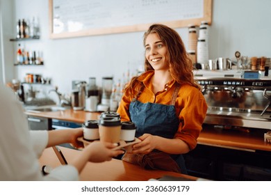 Takeaway food concept. A beautiful female barista gives to-go coffee to a client. Owner of a small business, a coffee shop,  behind the bar. Business concept. - Powered by Shutterstock