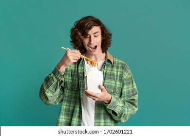 Takeaway Food Concept. Hungry Millennial Guy Eating Chinese Noodles From Disposable Box On Color Background, Copy Space