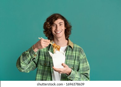 Takeaway Food. Happy Millennial Guy Eating Chinese Noodles From Disposable Box, Turquoise Background. Copy Space