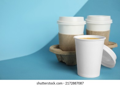 Takeaway paper coffee cups with sleeves, plastic lids and cardboard holder on blue background, space for text