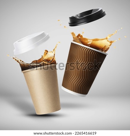Takeaway paper cups with splashing coffee falling on light grey background
