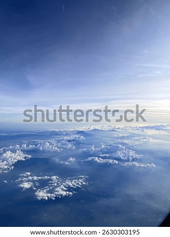 Taken from a plane window, the photo shows a vivid afternoon sky with hues of blue and white, fluffy clouds. Airplane turbine in view above mountain peaks.