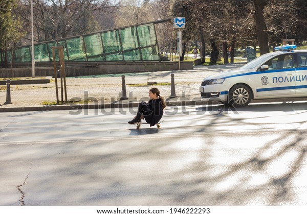 Taken in\
Sofia, Bulgaria in 27.03.2021. Girl rides a skateboard on the empty\
street, police car at the\
background
