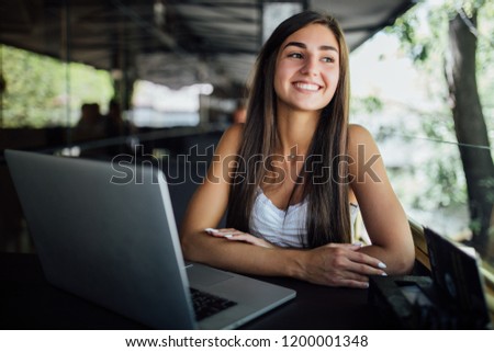 Taking advantages of free Wi-Fi. Beautiful young woman in funky hat working on laptop and smiling while sitting outdoors