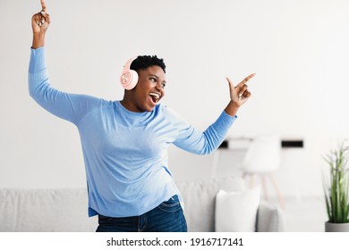 Taking Break. Overjoyed Millennial Plus-size Black Woman Wearing Wireless Headphones Dancing, Having Fun Moving And Listening To Music, Relaxing In Living Room, Enjoying Leisure Weekend At Home