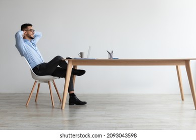 Taking Break. Profile Side View Of Smiling Young Arab Man Relaxing On Chair Sitting At Table And Using Laptop, Happy Millennial Male Leaning Back At Workplace, Looking At Pc Screen Watching Video