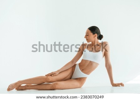 Taking a break, sitting on the floor. Young woman with slim body type is in fitness clothes in the studio.