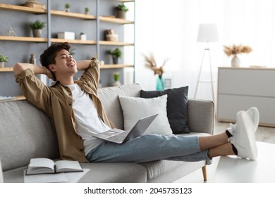 Taking Break. Smiling young asian man relaxing on comfortable couch in living room using pc laptop, happy millennial male resting on cozy sofa at home, leaning back, enjoying weekend or freelance job - Powered by Shutterstock