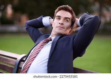 Taking a breather. A content businessman sitting with his hands behind his head on a park bench.