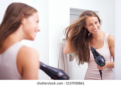 Taking Care Of Her Luscious Mane. A Young Woman Blow Drying Her Hair In Front Of A Mirror.