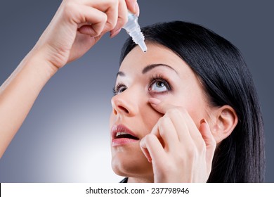 Taking Care Of Her Vision. Side View Of Young Women Applying Eye Drops While Standing Against Grey Background