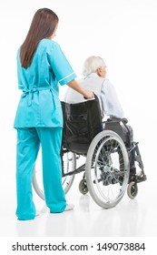 Taking Care Of Seniors. Rear View Of Confident Young Nurse Walking With Patient Sitting On The Wheelchair While Isolated On White