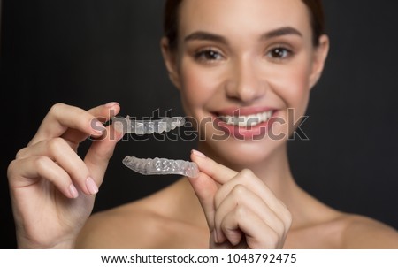 Taking care of teeth. Close up of clear aligners in hands of happy girl who is standing and showing orthodontic device to the camera. Selective focus and isolated background 商業照片 © 