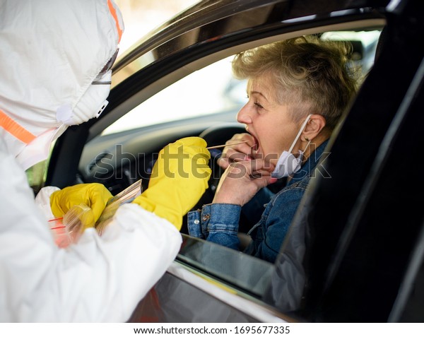 Taking corona virus test sample of senior woman\
in car, quarantine\
concept.
