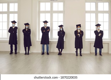 Taking Coronavirus Safety Measures And Graduating The New Normal Way During COVID-19 Pandemic. Diverse University Or College Students In Graduation Robes And Medical Face Masks Keeping Social Distance