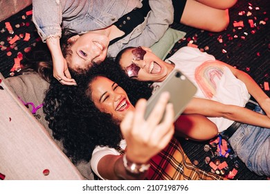 Taking Crazy Overhead Selfies. Top View Of Three Happy Friends Taking A Selfie While Lying On The Floor At A House Party. Group Of Cheerful Female Friends Having Fun Together On The Weekend.