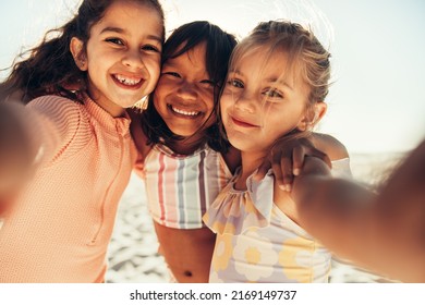 Taking cute summer selfies at the beach. Three happy little girls smiling for a group selfie by the seaside. Group of adorable little children having fun together during summer vacation. - Powered by Shutterstock