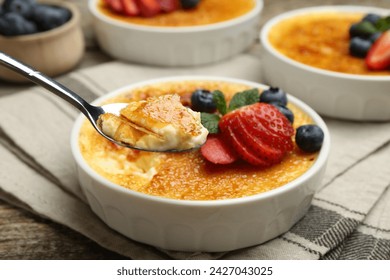 Taking delicious creme brulee with berries and mint from bowl at wooden table, closeup - Powered by Shutterstock