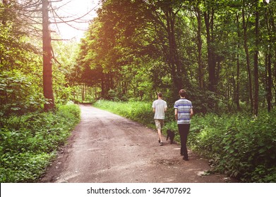 Taking The Dog Out For A Walk In The Woods. Two Brothers Walking The Dog Through The Forest. Spending Time Outdoors In Nature And Relaxing Together- Lifestyle Image With A Warm Filtered Vintage Look