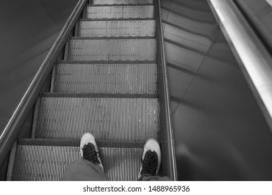 Taking the down escalator and moving to the platform of metro stations. Down view under feet on sneakers.