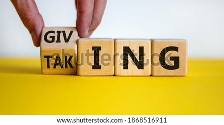 Taking or giving symbol. Hand turns a cube and changes the word 'taking' to 'giving' on wooden cubes. Beautiful yellow table, white background, copy space. Business and taking or giving concept.