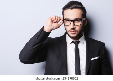 Taking life seriously. Portrait of handsome young man in formalwear adjusting his glasses while standing against grey background - Powered by Shutterstock