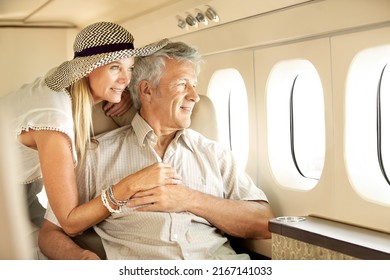 Taking a luxury trip. Smiling senior couple on an airplane looking out the window.