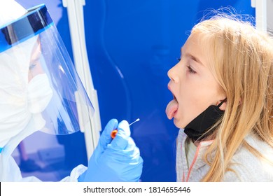 Taking A Medical Sample - A Throat Swab For A Coronavirus Test. Nurse Wearing Protective Suit For Working With Biohazard Takes A Sample From 
 Child Blond Girl Open Mouth