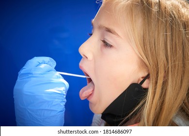 Taking A Medical Sample - A Throat Swab For A Coronavirus Test. Nurse Wearing Protective Suit For Working With Biohazard Takes A Sample From 
 Child Blond Girl For Covid 19 Test