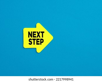 Taking The Next Step In Business, Career Or Education Concept. Yellow Arrow Shaped Sticker With The Message Next Step On Blue Background.