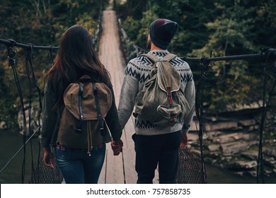 Taking Next Step. Rear View Of Young Couple Stepping On The Suspension Bridge While Hiking Together In The Woods