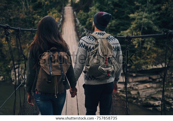 Taking next\
step. Rear view of young couple stepping on the suspension bridge\
while hiking together in the\
woods