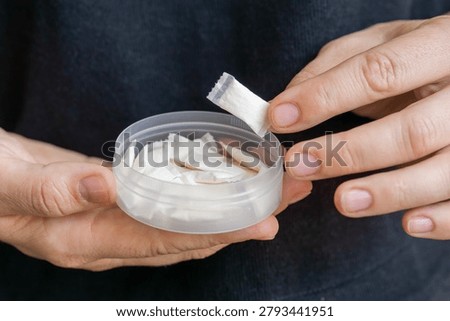 taking nicotine pouch background plastic box surface close up of hands holding white snus portion swedish tobacco free alternative smokeless product concept of addiction, bad habits, nicotine delivery