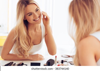 Taking Off Her Make-up. Beautiful Cheerful Young Woman Using Cotton Disk And Looking At Her Reflection In Mirror With Smile While Sitting At The Dressing Table