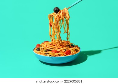 Taking pasta with a fork from a bowl, minimalist on a green table. Vegan Italian dish, spaghetti puttanesca, with tomato sauce, black olives, and capers. - Powered by Shutterstock