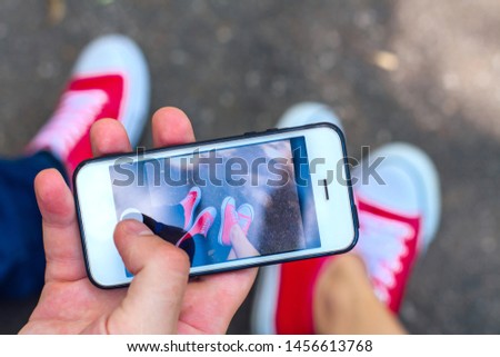 Taking photo with mobile phone of red sneakers shoes on woman's and man's feet. Sneakers shoes Couple. Copy space.