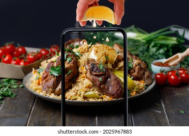 Taking Photo On Smartphone Female Hands Press Lemon Juice On Pilaf With Lamb Meat In Plate On Wooden Table, Black Background.