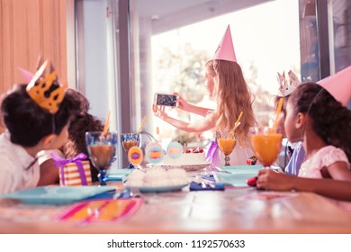 Taking photos. Long haired careful girl standing with modern smartphone and taking selfies with her friends at the party - Powered by Shutterstock