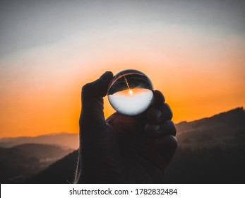 Taking photos of sunset through the small glass ball holding in hand