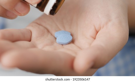 Taking pills. Two big blue diamond-shaped pills labeled 100 fall into palm of hand from pill bottle. Close-up, front view, center composition - Shutterstock ID 1923506147